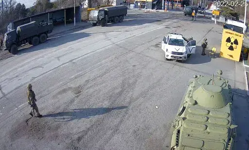 A frame grab taken by the battery-operated camera placed by Chernobyl Tour to show the company’s tourist information center near the Chernobyl nuclear power plant, shows Russian military vehicles rolling into Chernobyl, the site of the world's worst nuclear disaster, on the second day of the war, in the village of Dytyatki, Ukraine, on Friday, Feb. 25, 2022. (Yaroslav Yemelianenko/Chernobyl Tour via AP)