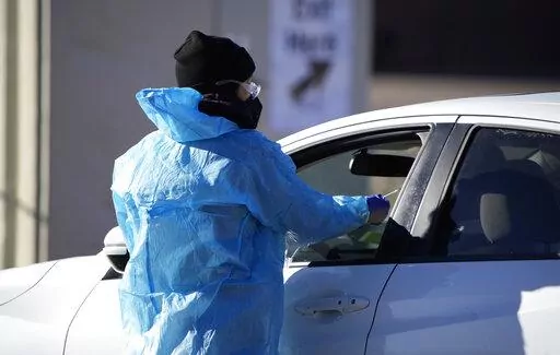 A medical technician performs a nasal swab test on a motorist queued up in a line at a COVID-19 testing site near All City Stadium Dec. 30, 2021, in southeast Denver. Millions of workers whose jobs don’t provide paid sick days are having to choose between their health and their paycheck as the omicron variant of COVID-19 rages across the nation. While many companies instituted more robust sick leave policies at the beginning of the pandemic, those have since been scaled back with the rollout o