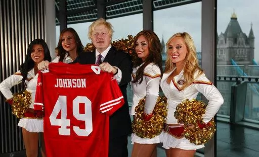 Boris Johnson, then Mayor of London center, and four of the 49ers cheerleaders Deanna Ortega, left, Morgan McLeod, Alexis Kofoed and Lauren Riccaboni, right, pose for the media as the Mayor holds a team shirt with his name on at City Hall in London Tuesday, Oct., 26, 2010. British media say Prime Minister Boris Johnson has agreed to resign on Thursday, July 7 2022, ending an unprecedented political crisis over his future. (AP Photo/Alastair Grant, File)
