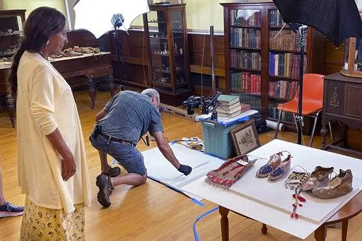Leola One Feather, left, of the Oglala Sioux Tribe in South Dakota, observes as John Willis photographs Native American artifacts on July 19, 2022, at the Founders Museum in Barre, Massachusetts. The private museum, which is housed in the town library, is working to repatriate as many as 200 items believed to have been taken from Native Americans massacred by U.S. soldiers at Wounded Knee Creek in 1890. Willis is photographing the items for documentation, ahead of their expected return to the tr