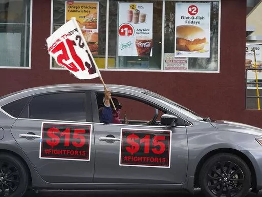 FILE - Fast-food workers drive though a McDonald's restaurant demanding a for a $15 hourly minimum wage in East Los Angeles Friday, March 12, 2021. Minimum wage increases, animal protections, police accountability, cutting and increasing taxes are all part of a series of new laws taking effect across the country on Saturday, the first day of 2022. (AP Photo/Damian Dovarganes, File)