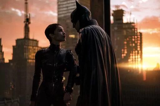 This image released by Warner Bros. Pictures shows Zoe Kravitz, left, and Robert Pattinson in a scene from "The Batman."  “The Batman” is still going strong three weeks into its theatrical run, with a tight grip on the top spot at the box office. Robert Pattinson’s debut as the Dark Knight earned an additional $36.8 million over the weekend, according to studio estimates Sunday, March 20, 2022. It also slid past the $300 million mark ahead of projections. (Jonathan Olley/Warner Bros. Pictu