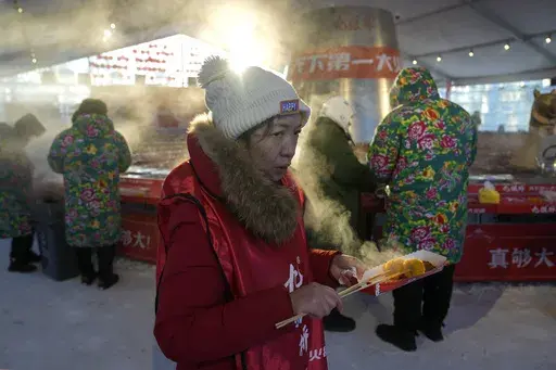 A woman eats hot food to keep warm at a giant hotpot restaurant inside the Harbin Ice and Snow World in Harbin in China's Heilongjiang province, Monday, Jan. 6, 2025. (AP Photo/Andy Wong)